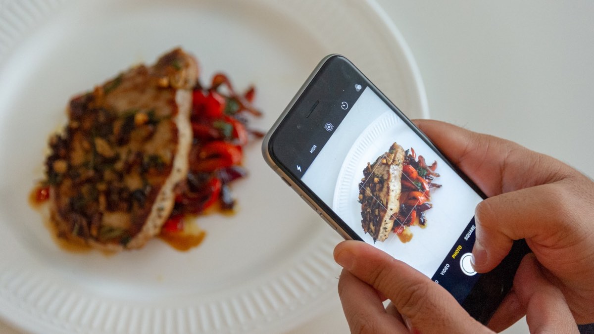 A phone photographing a plated dish on a white plate in daylight